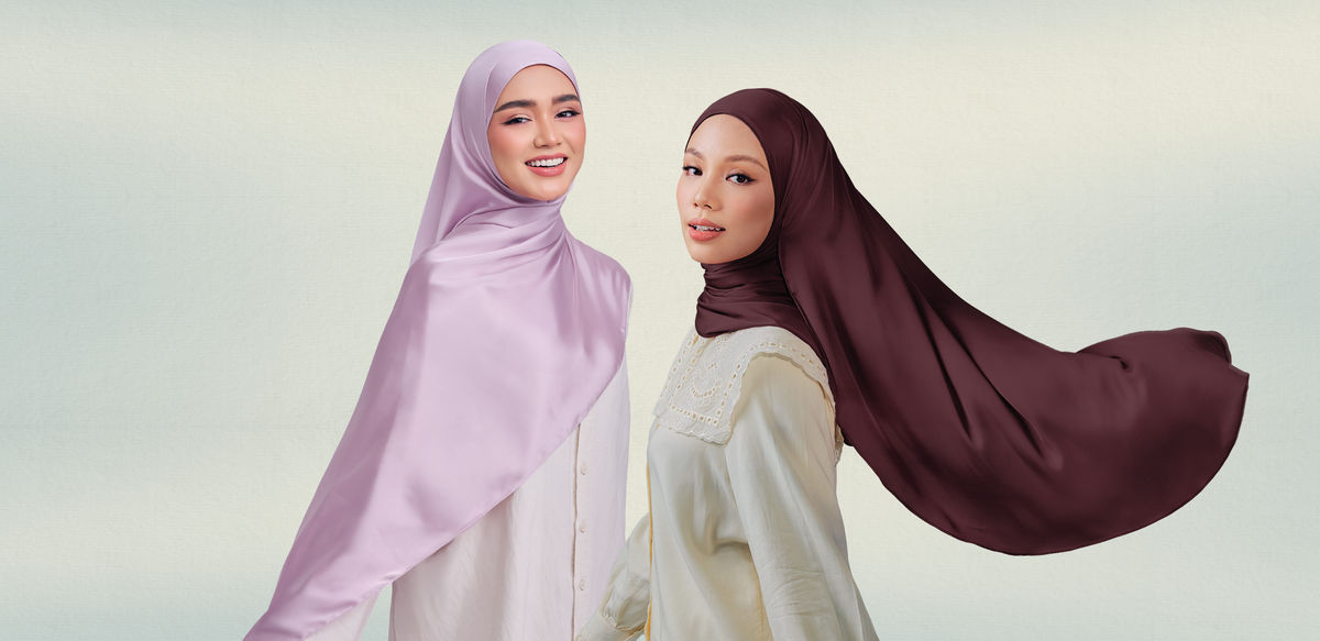 Two women in long satin shawls, one pale lilac and one deep plum, with the plum shawl's end flowing in the air